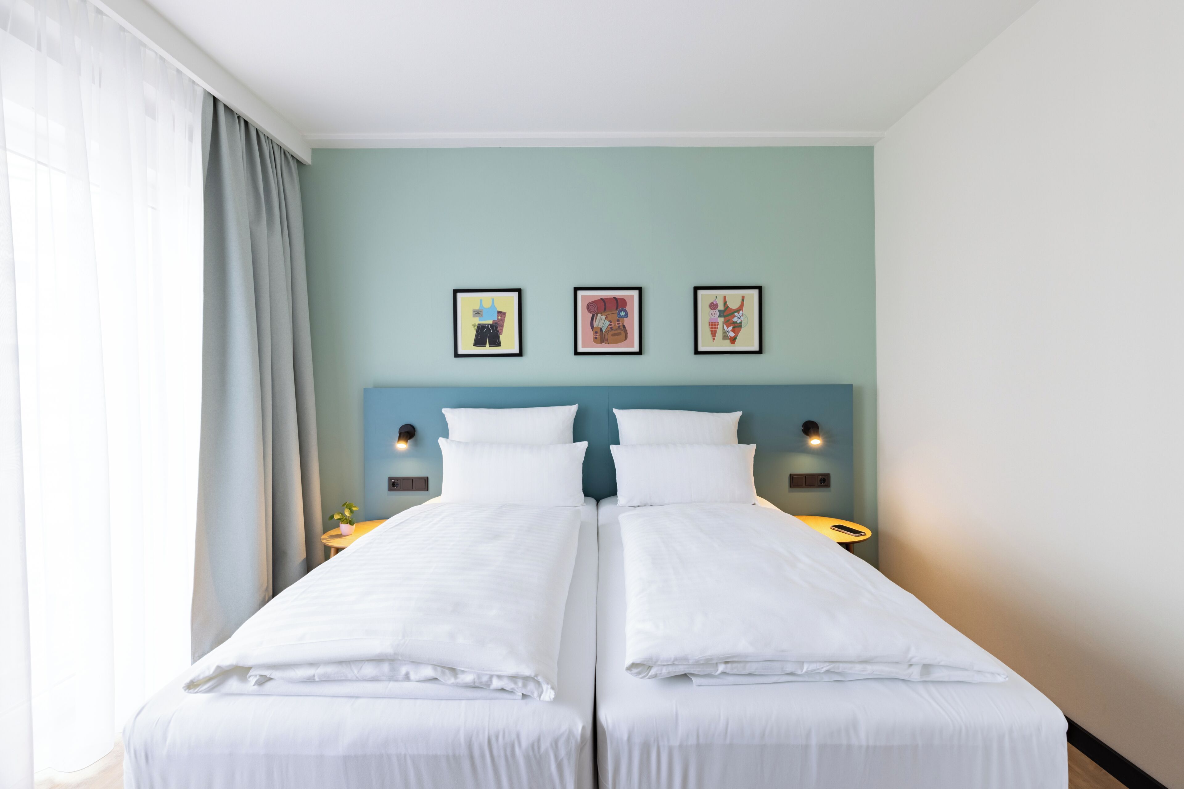 A double bed with white linens, two bedside tables, and three framed artworks on the wall.