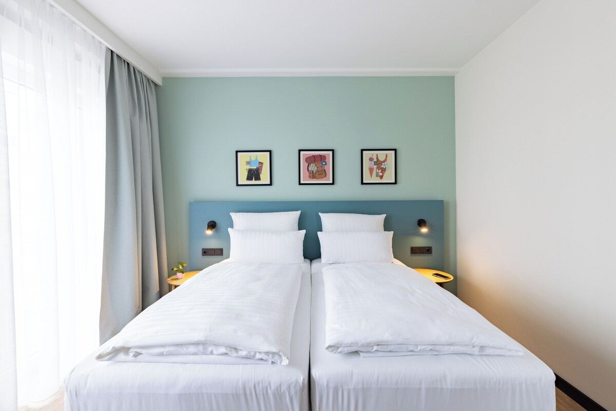 A double bed with white linens, two bedside tables, and three framed artworks on the wall.