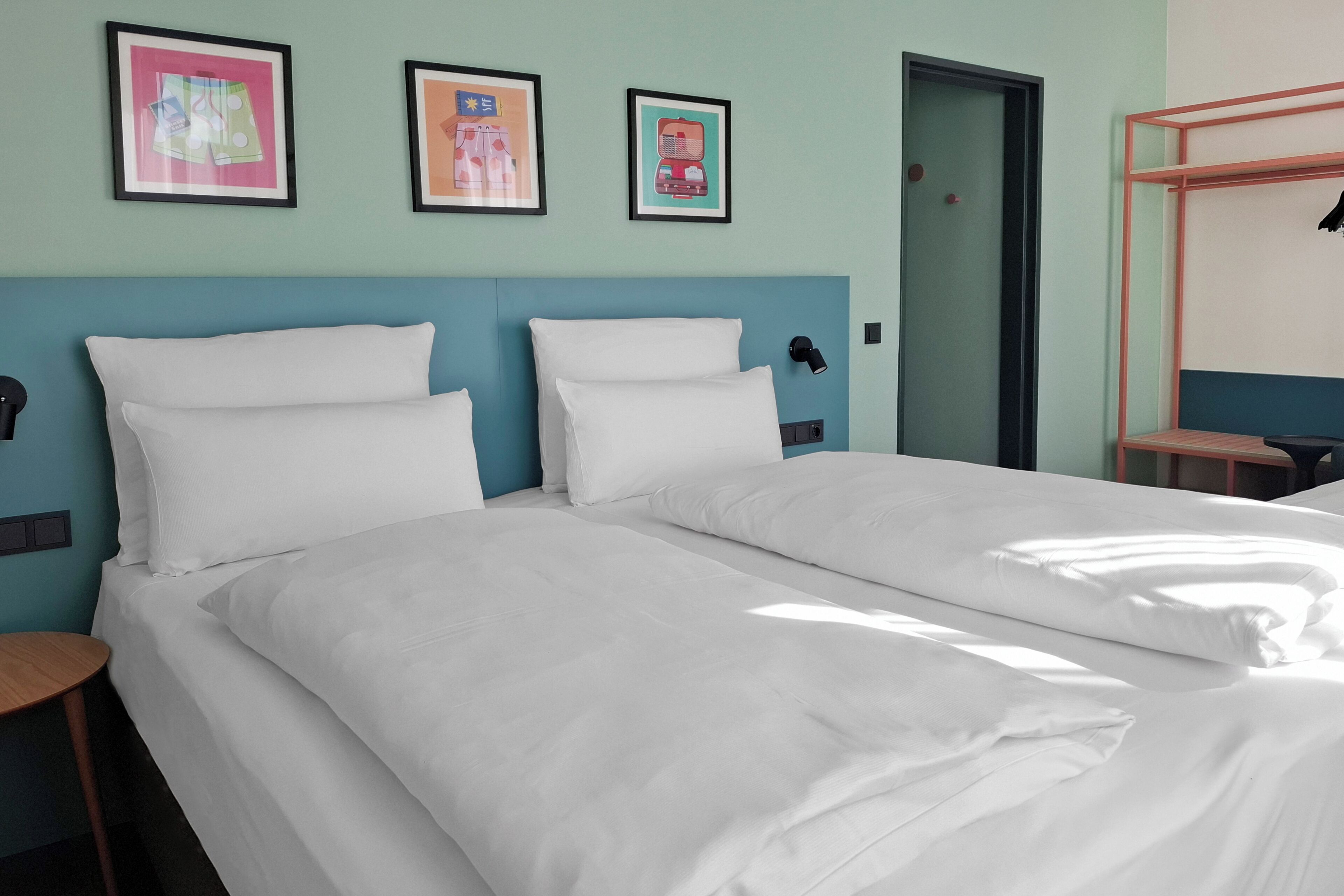 Habitación de hotel con dos camas, una puerta y cuadros en la pared.