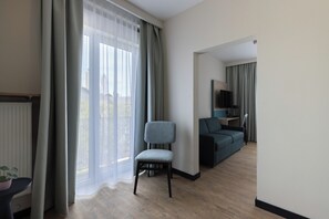 A modern living room with a wooden floor, a grey upholstered chair, a dark sofa, and a television on a stand.