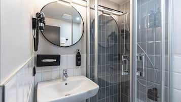 Ein modernes Badezimmer mit einem weißen Waschbecken, einem runden Spiegel, einer Handbrause und einer Duschkabine aus Glas.