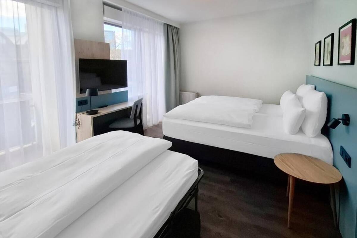 A hotel room with two beds, a desk with a computer, a TV, and a small round table.