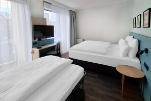 A hotel room with two beds, a desk with a computer, a TV, and a small round table.