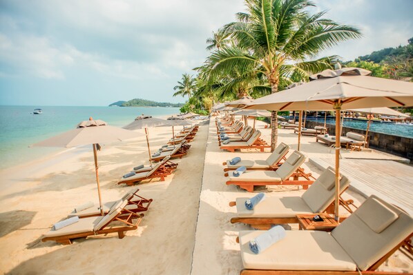 A beach with rows of sun loungers under umbrellas, a pool, and palm trees. - InterContinental Koh Samui Resort by IHG (Koh Samui)