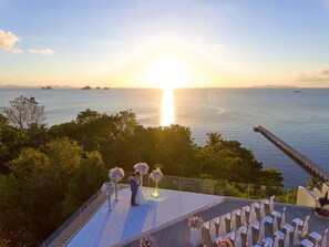 A wedding ceremony on a rooftop with a view of the ocean and islands at sunset.