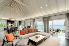 A spacious living room with a large sofa, a coffee table, and a dining area with a view of the ocean.
