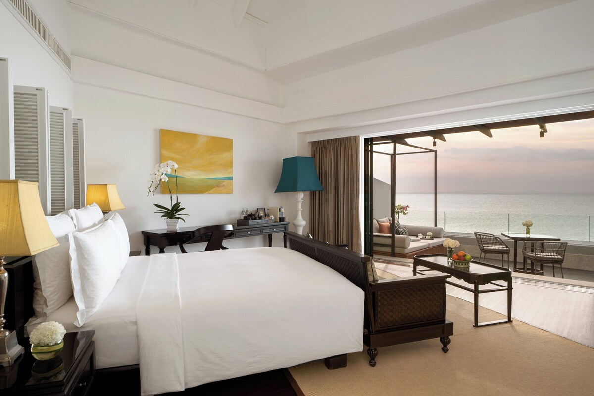 Une chambre d’hôtel avec un grand lit, un bureau, une chaise et un balcon donnant sur l’océan.
