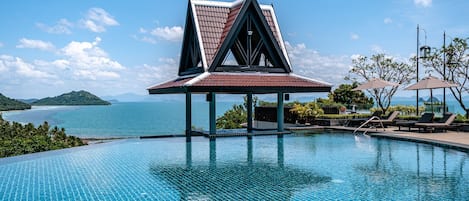 A swimming pool with a triangular pavilion, lounge chairs, and a view of the sea.