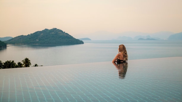 Une personne est assise au bord d’une piscine à débordement, d’où l’on peut admirer un plan d’eau paisible et des îles lointaines.