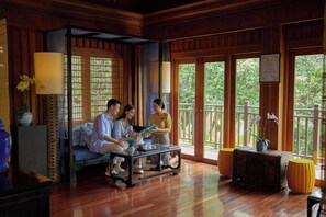 A room with a wooden floor, a sofa, a table with a vase, and a window with a view of greenery.