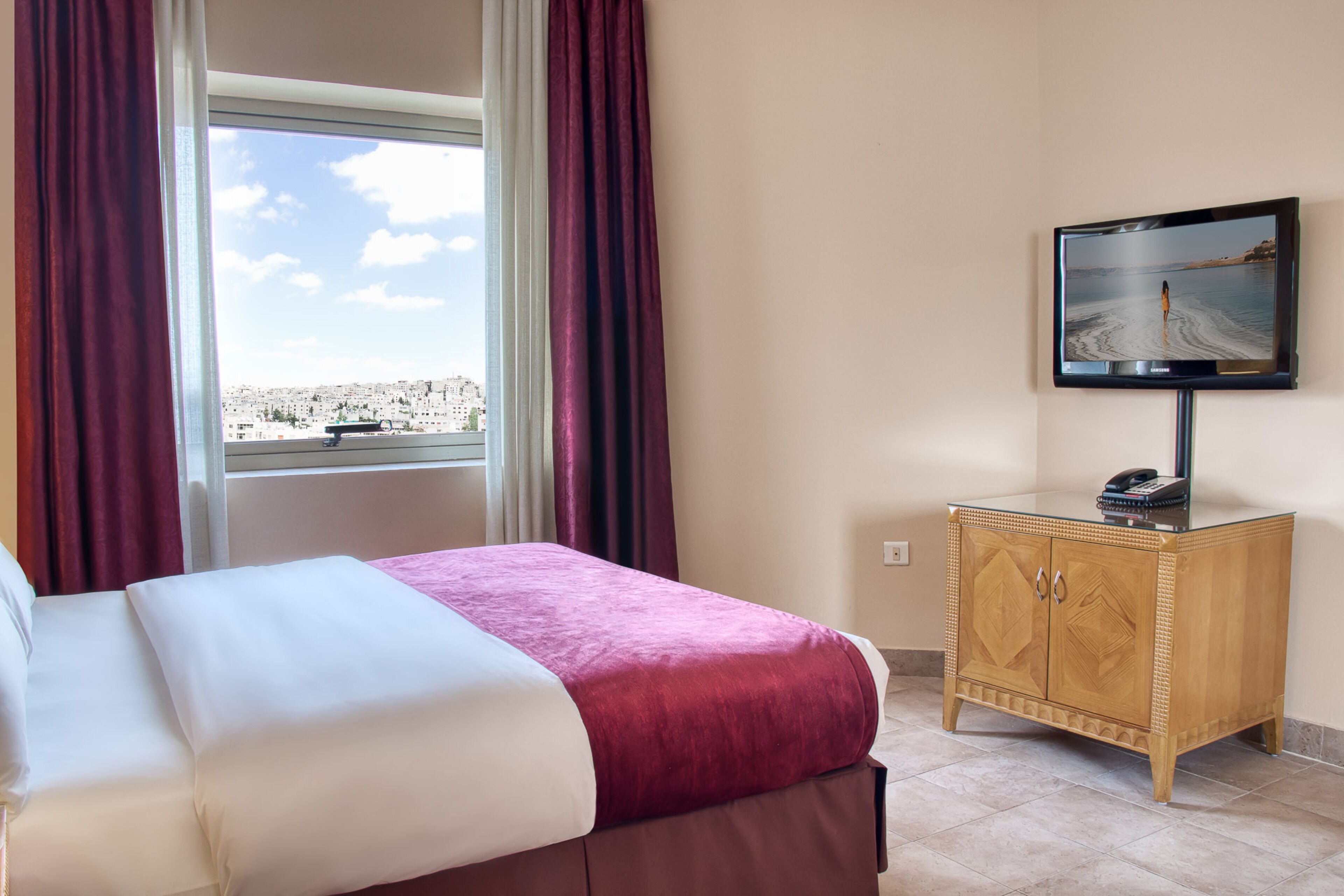 A hotel room with a bed, a television mounted on the wall, a wooden cabinet, and a window with curtains.
