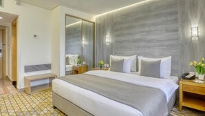 Una habitación de hotel con una cama grande, una mesita de noche con lámpara, un espejo y un pequeño banco.