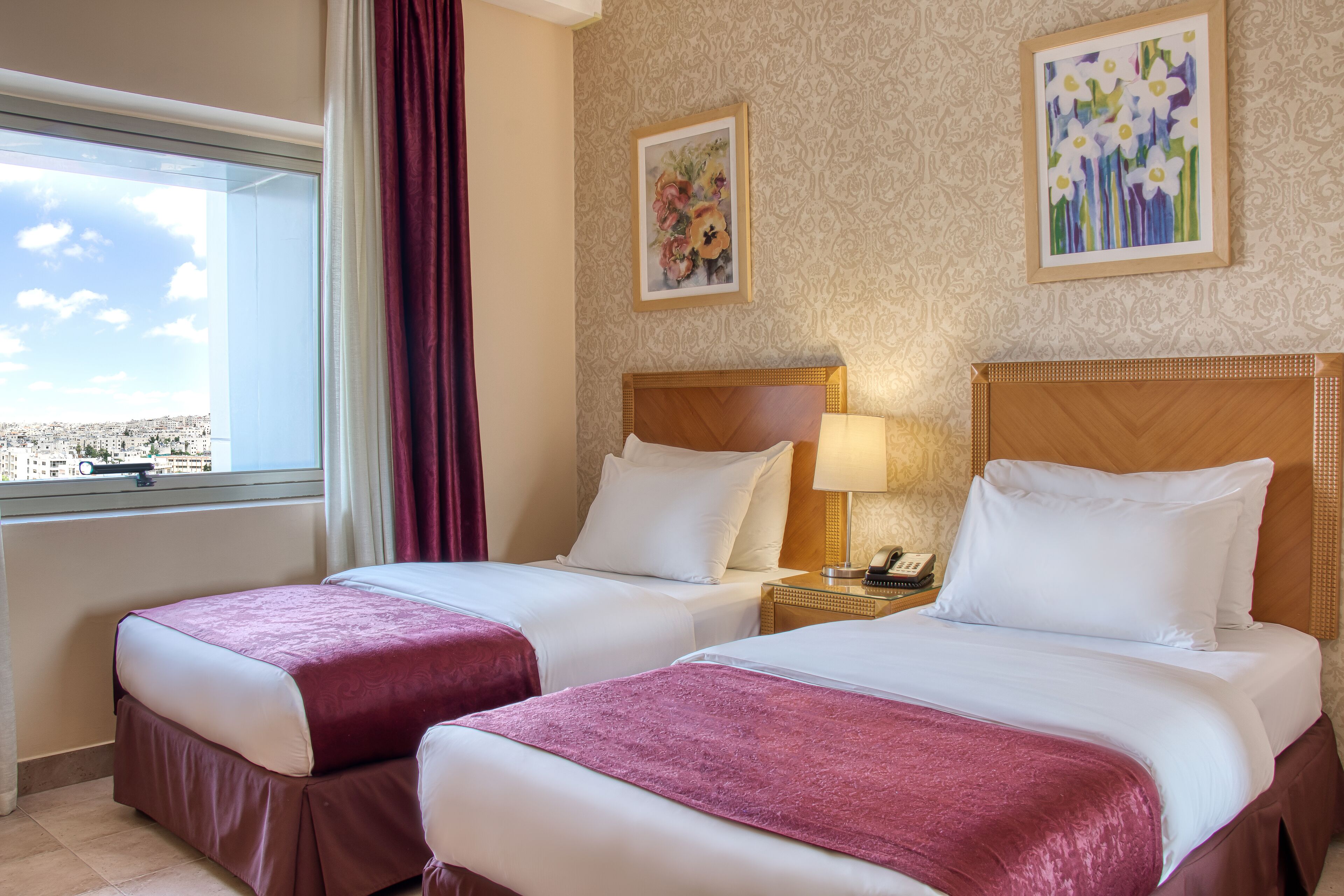 A hotel room with two beds, a window with a view, and artwork on the walls.