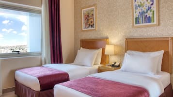 A hotel room with two beds, a window with a view, and artwork on the walls.