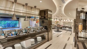 Un área de desayuno moderno en un hotel, con un sistema de buffet que incluye diversos recipientes de comida y una estación de café.