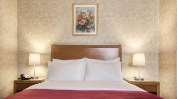 A hotel room with a large bed, two bedside tables with lamps, a telephone, and a framed floral artwork on the wall.