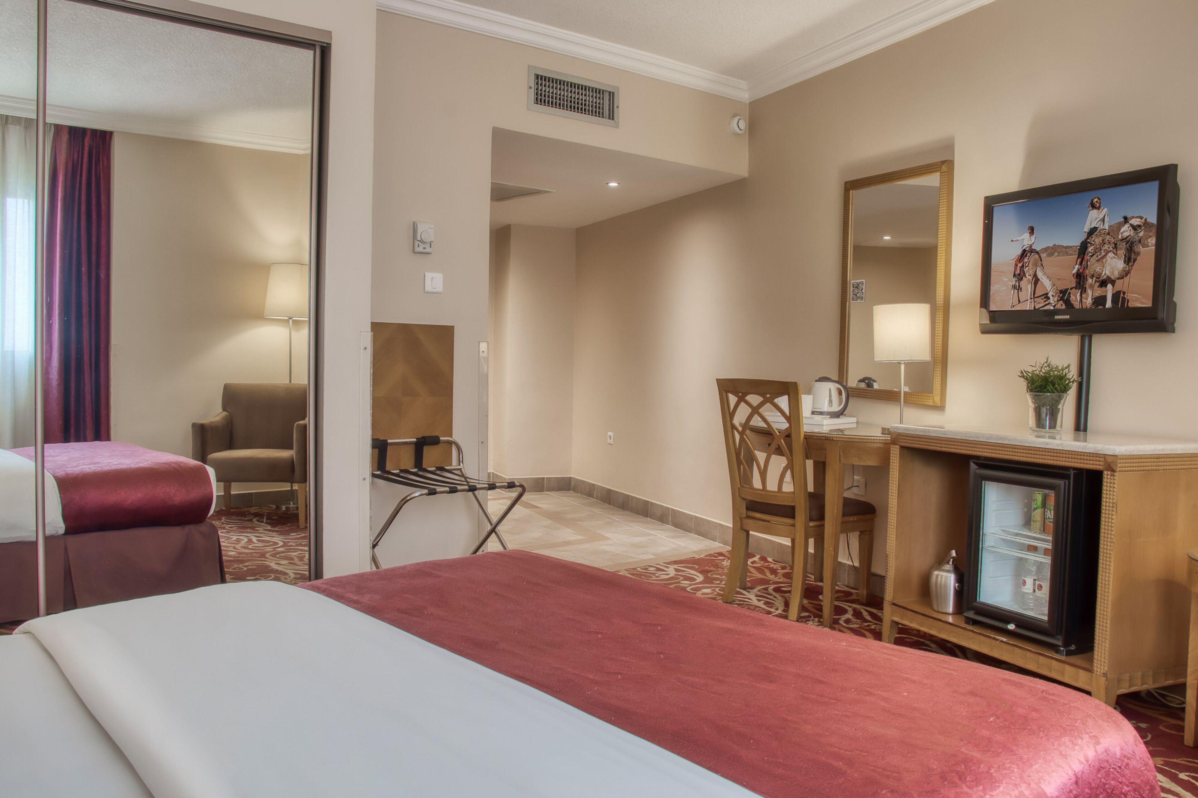 Een hotelkamer met een bed, bureau, stoel, televisie en een koelkast.