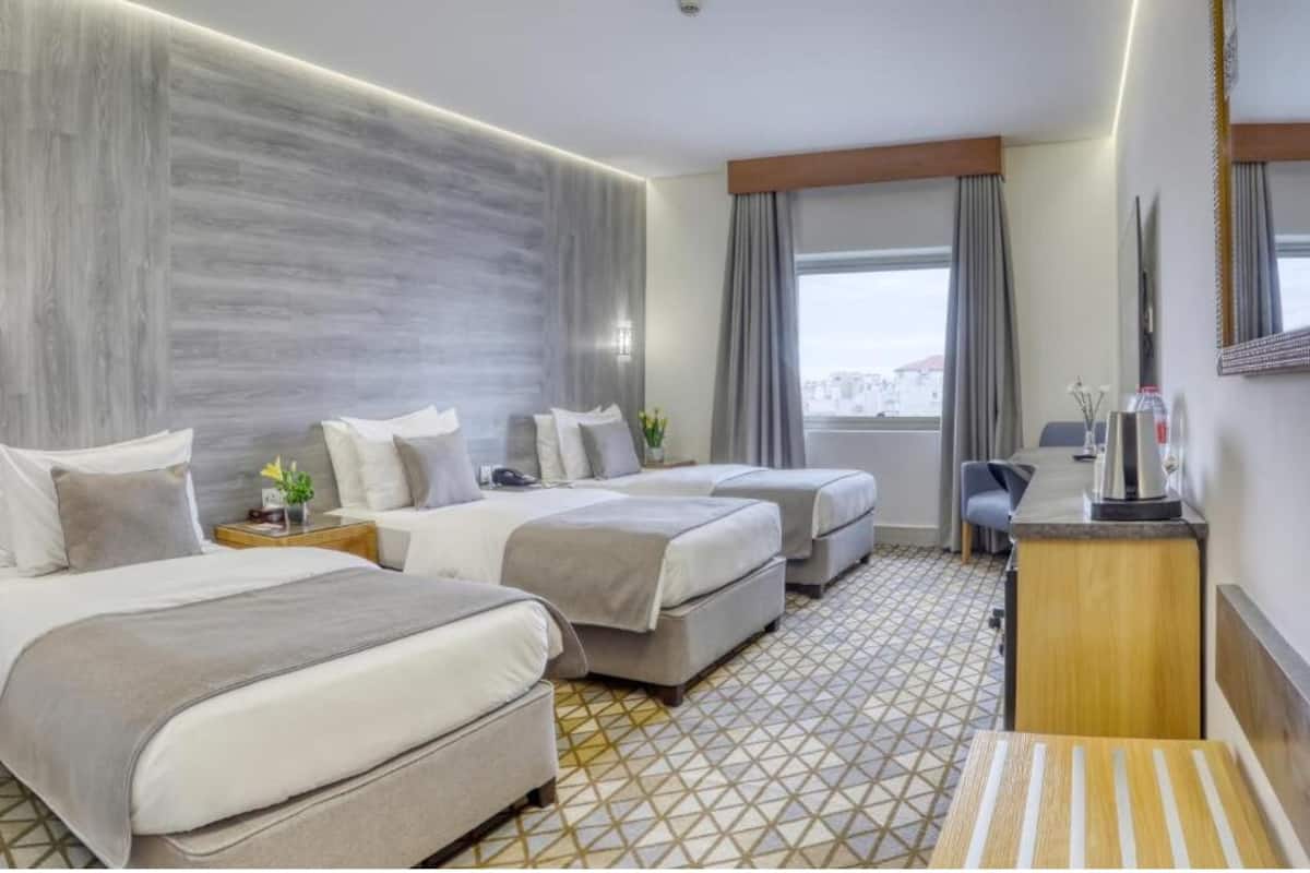 A hotel room with two beds, a desk, a chair, a TV, and a window with curtains.