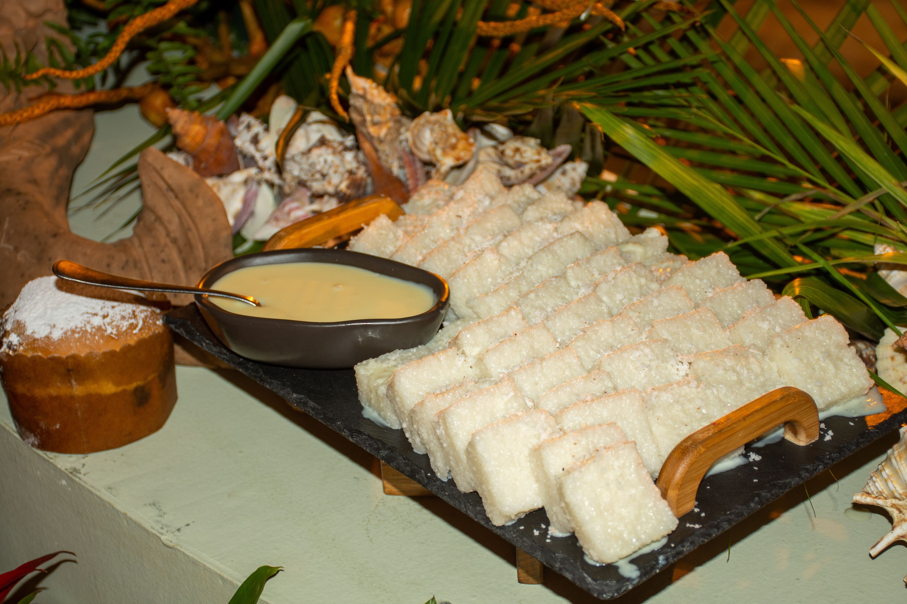 A dessert platter with a bowl of sauce and a dusted pastry on a slate serving board.
