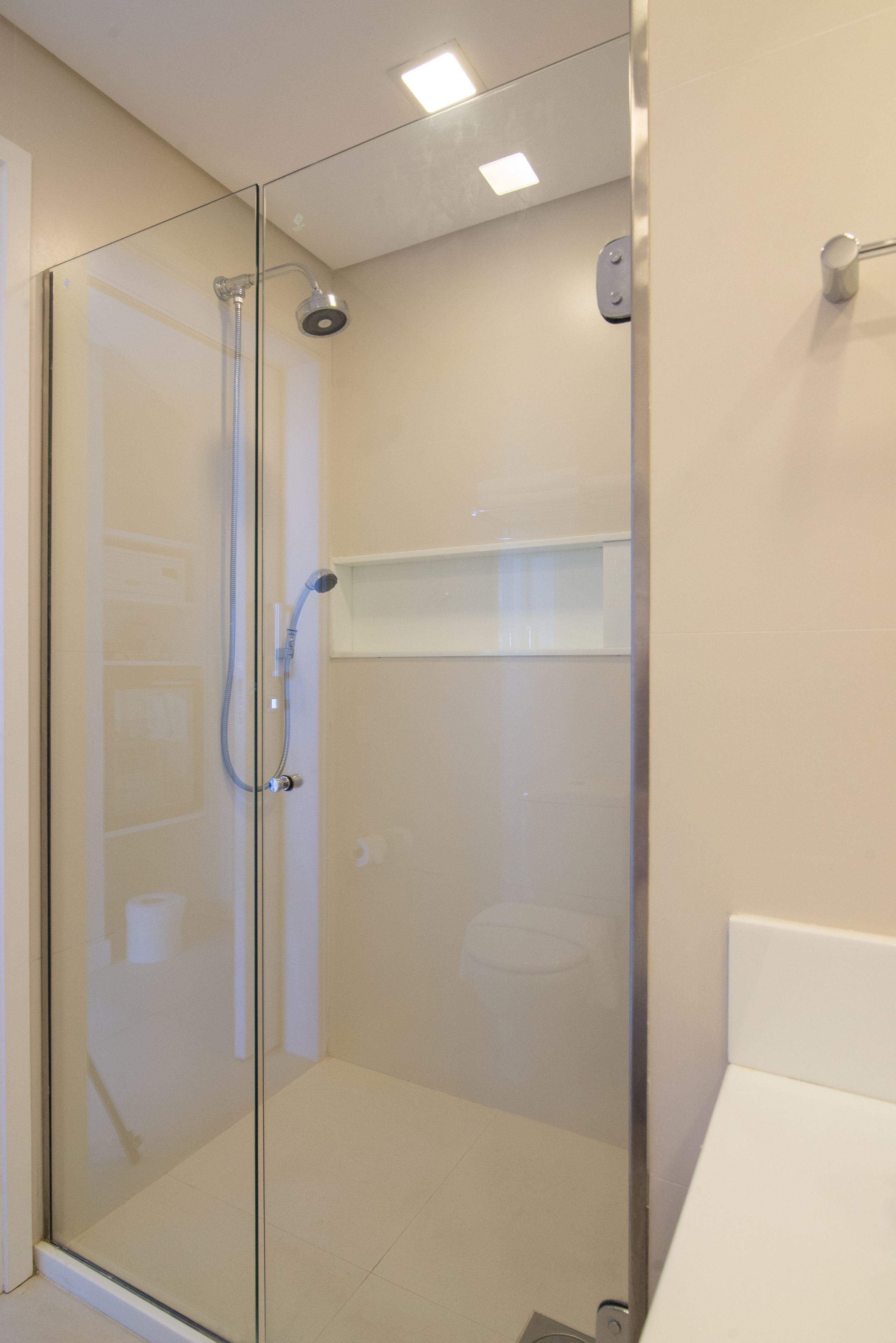 Un baño moderno con ducha envuelta en vidrio, un lavabo blanco y un estante pequeño encima.