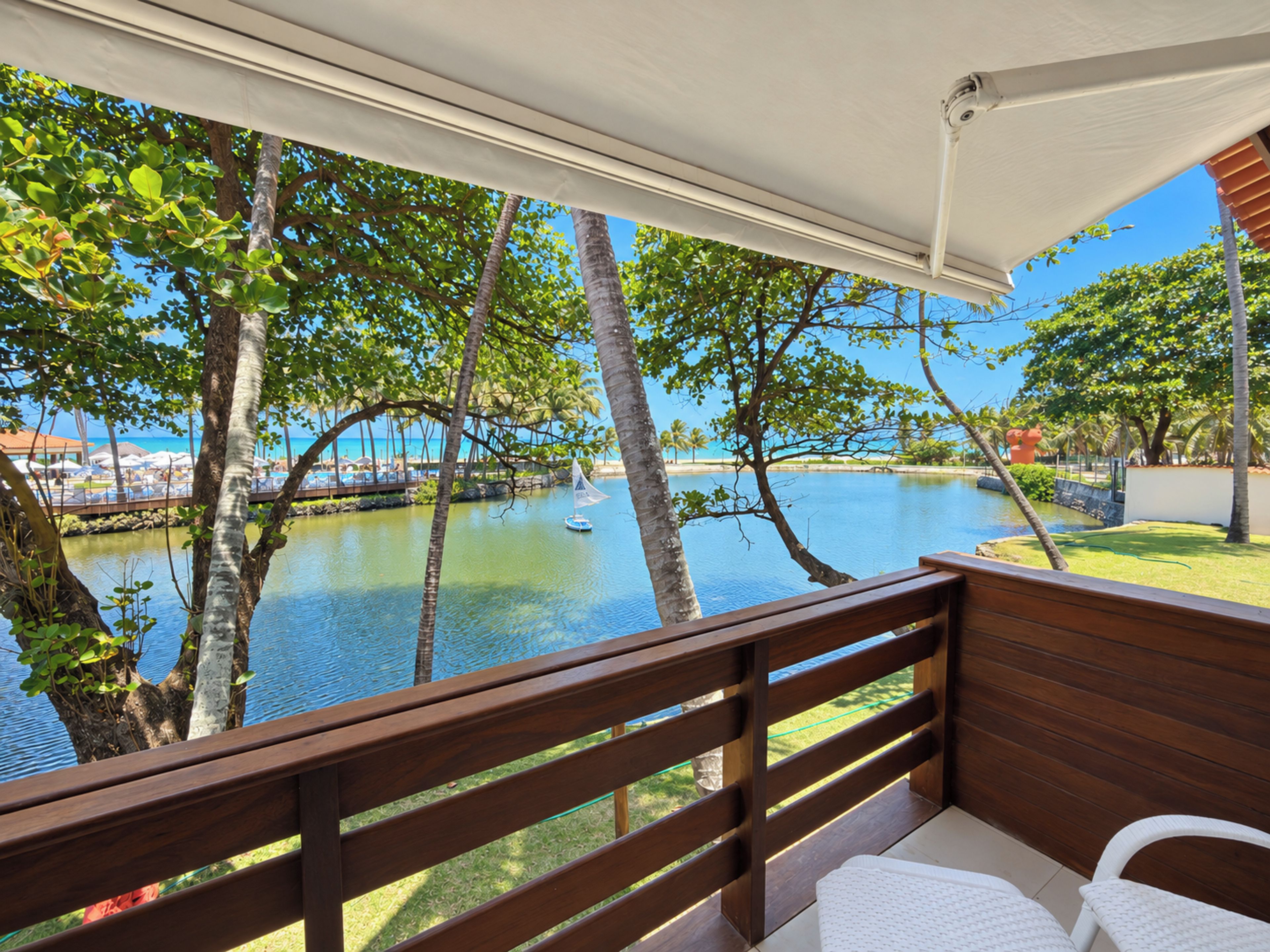 Una terraza de madera con vistas a un cuerpo de agua tranquilo, palmeras y una costa lejana.