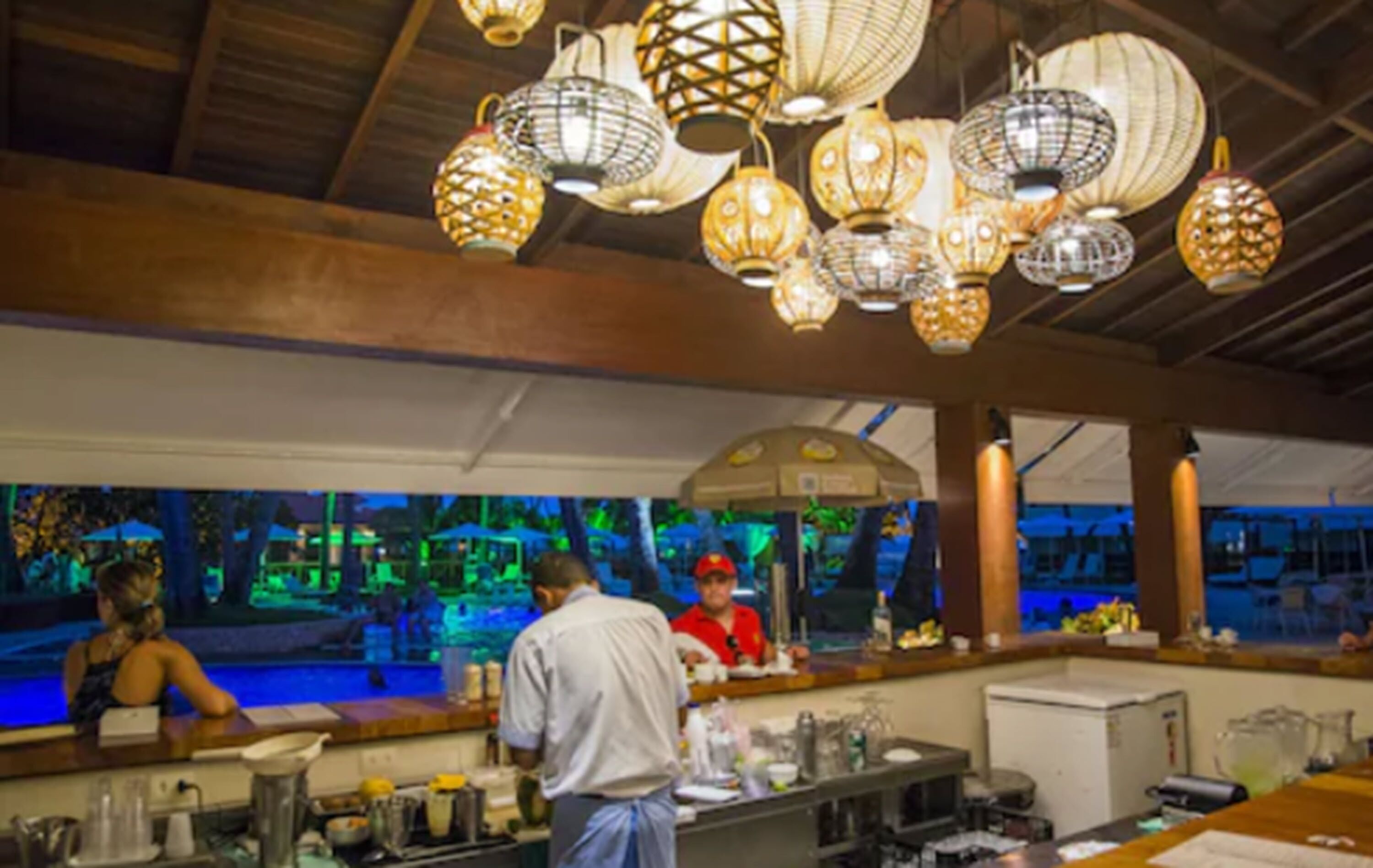 A restaurant with a bar area, wooden ceiling, and hanging lanterns.