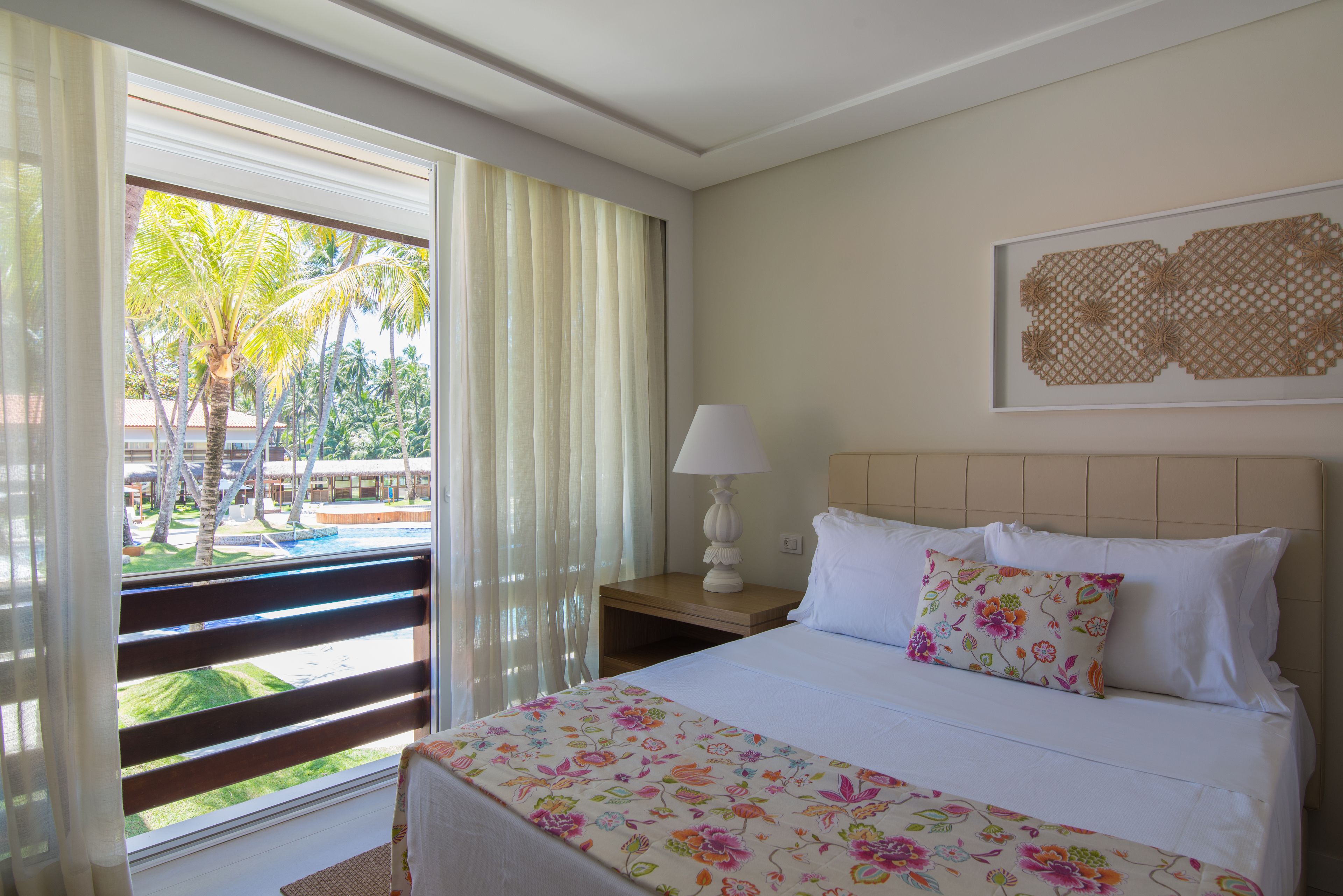 Una habitación de hotel con cama, mesita de noche, lámpara, ventana con cortinas y una obra de arte colgada en la pared.