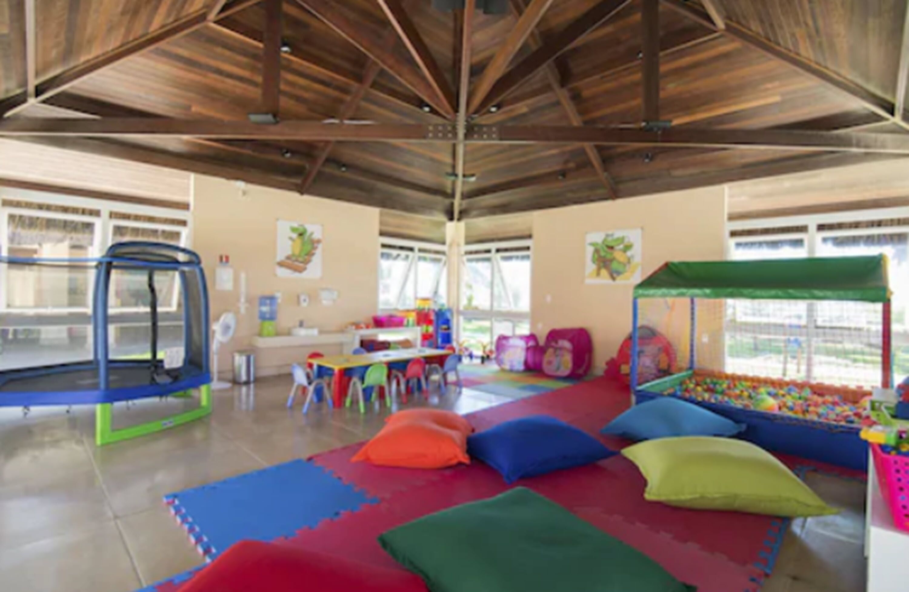 Un área de juegos interior amplia con un trampolín, coloridos tapetes de juego y una piscina de pelotas.