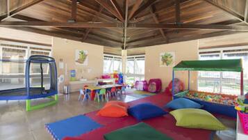 Un área de juegos interior amplia con un trampolín, coloridos tapetes de juego y una piscina de pelotas.