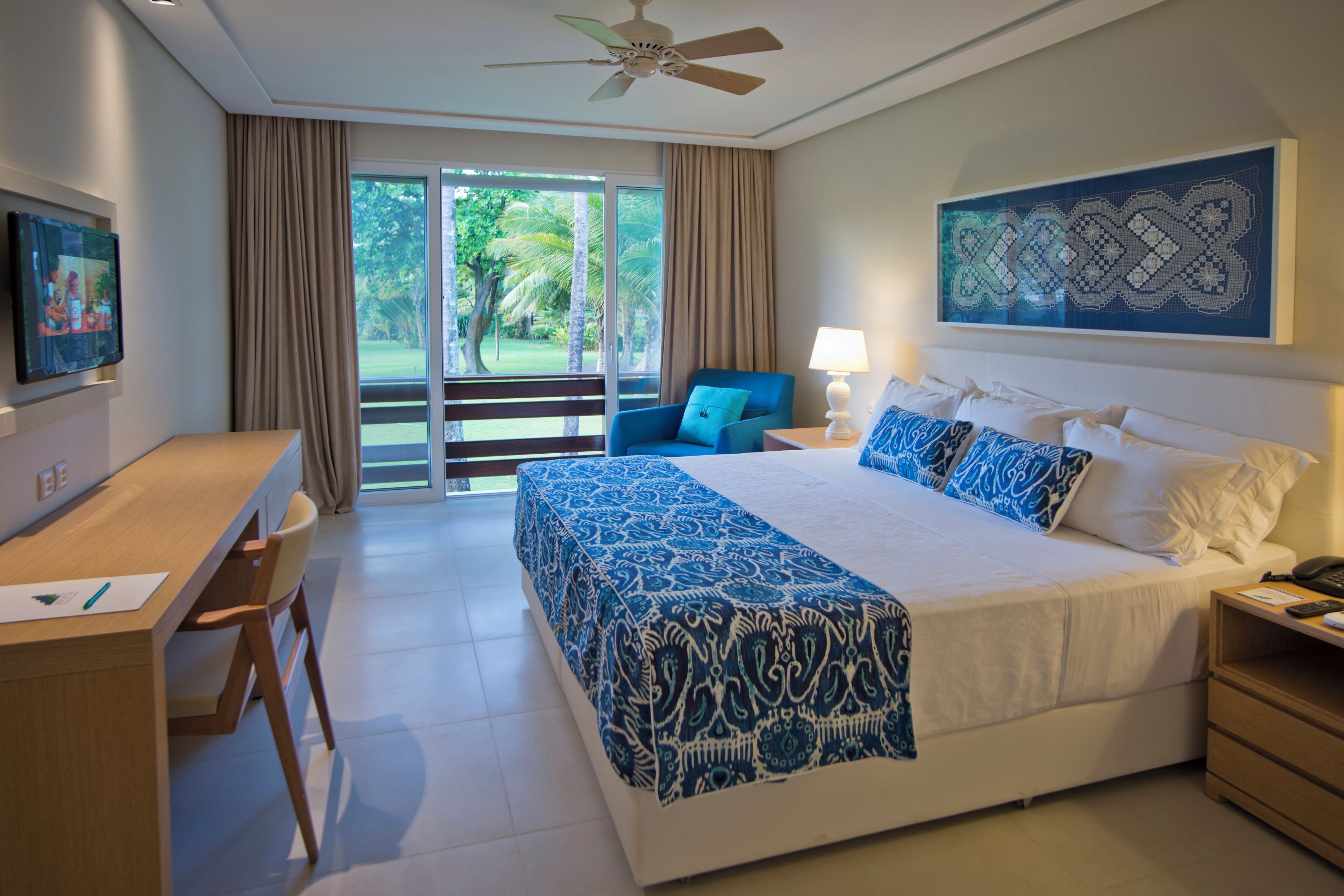A hotel room with a bed, desk, chair, and a view of the outdoors.