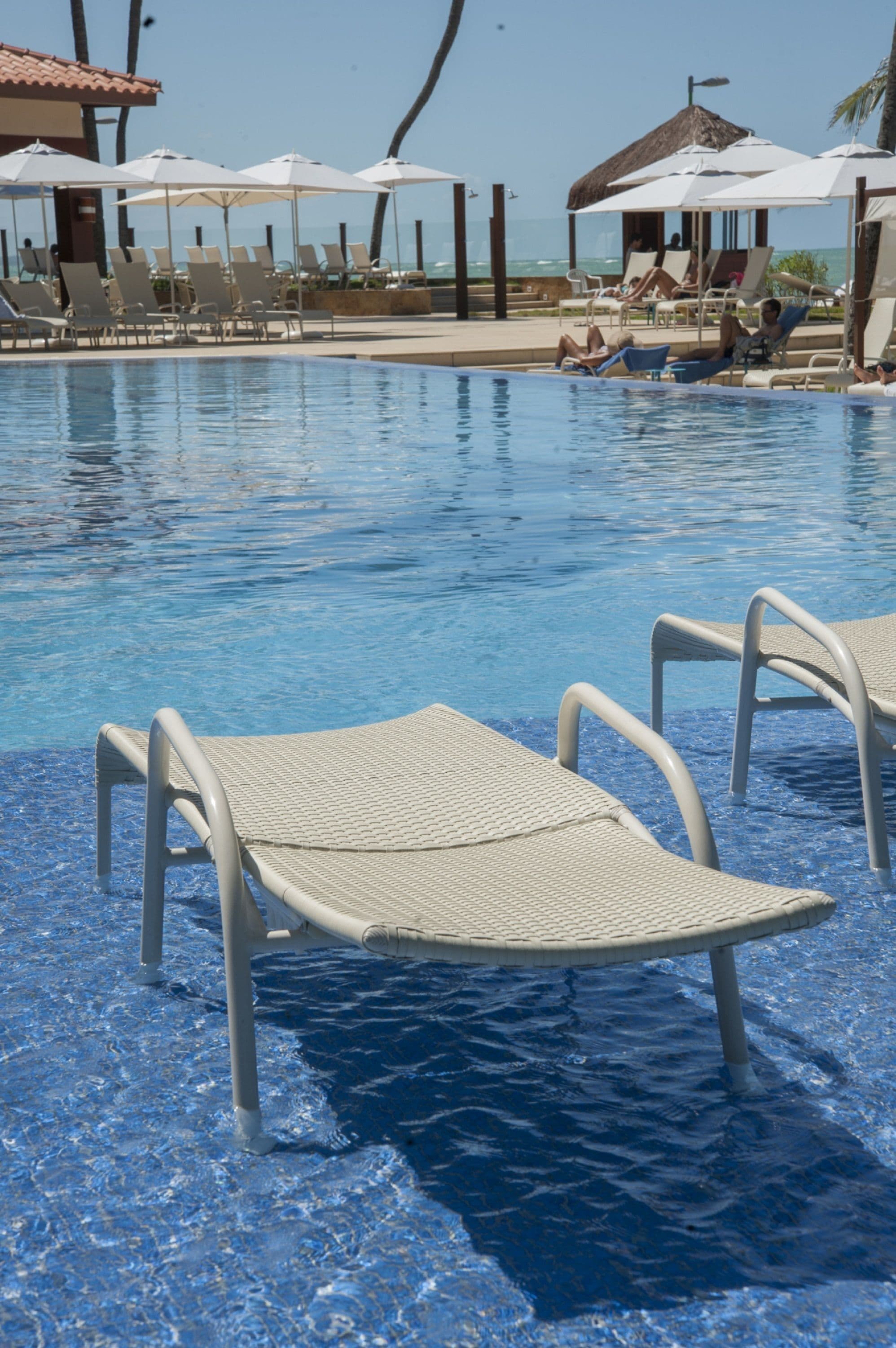 A pool area with lounge chairs and umbrellas, a clear blue pool, and a view of the ocean.