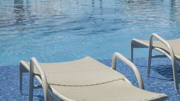 A pool area with lounge chairs and umbrellas, a clear blue pool, and a view of the ocean.