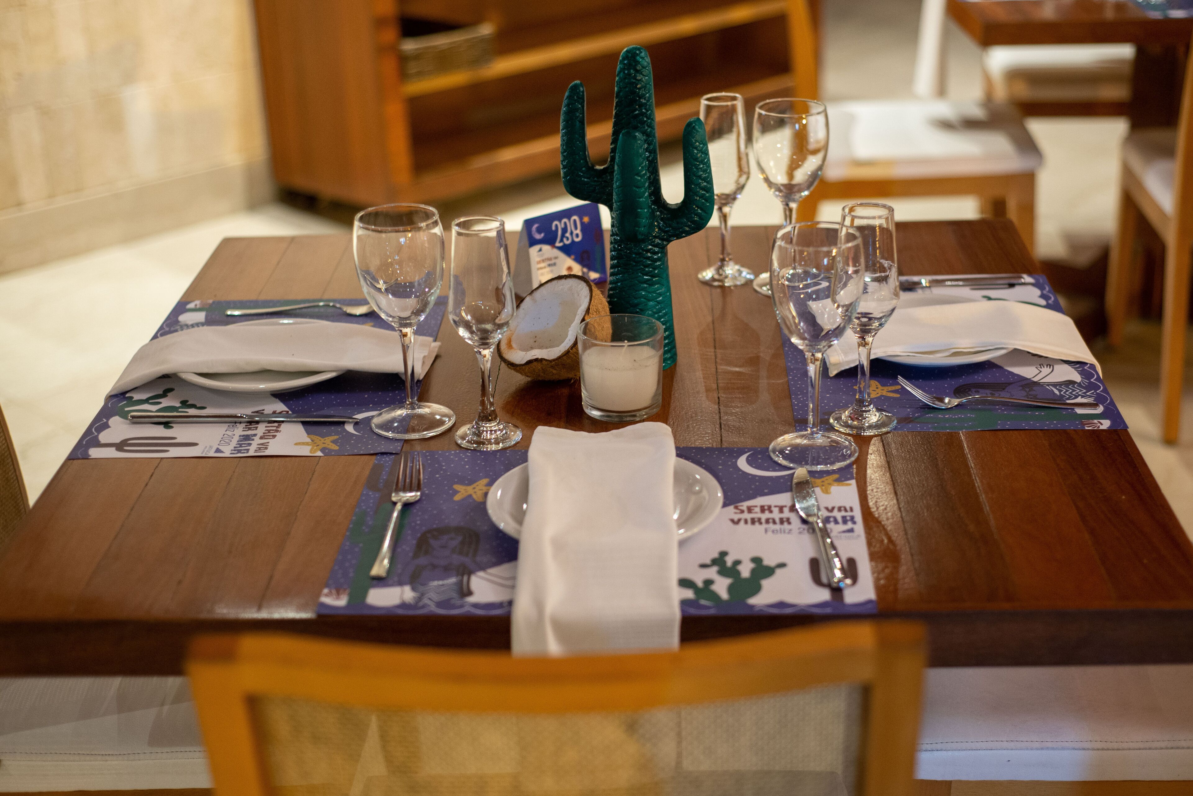 Una mesa de comedor servida con copas de vino, platos y un cactus como centro de mesa.
