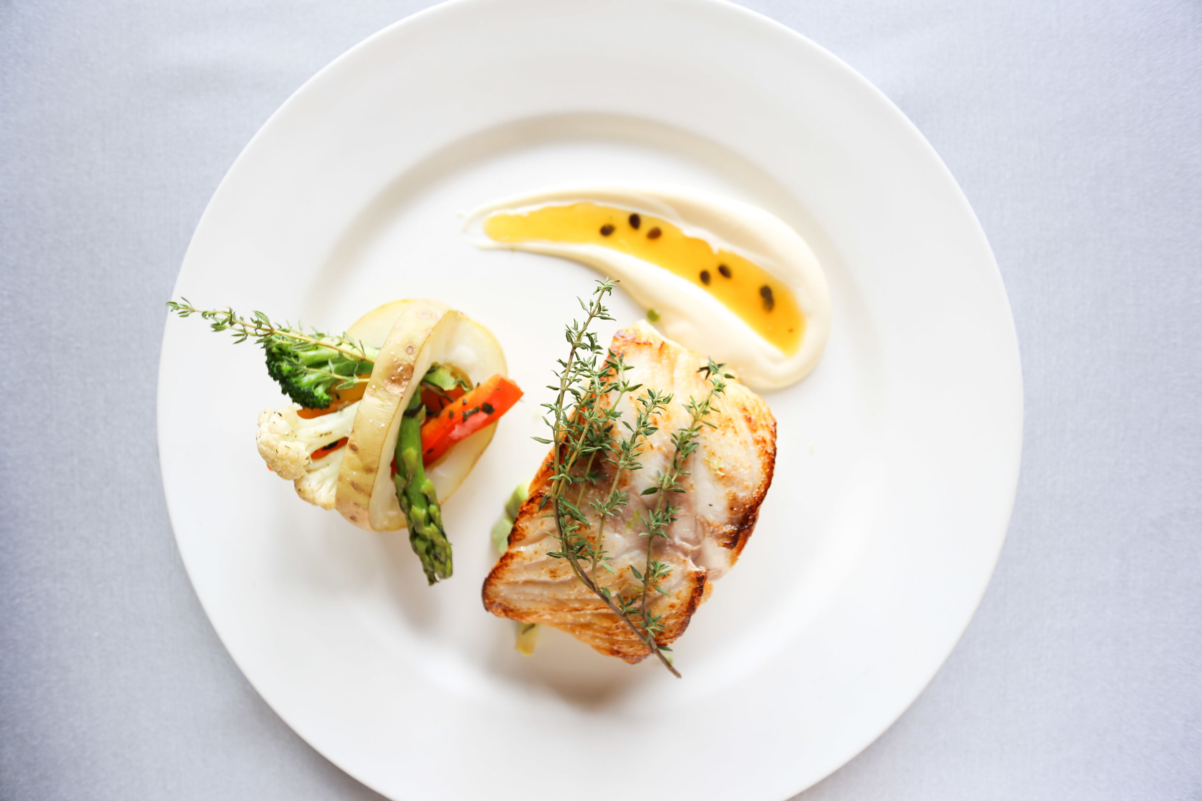 A white plate with a piece of grilled fish, asparagus, and a slice of lemon.