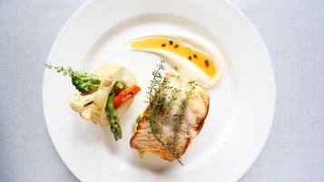 A white plate with a piece of grilled fish, asparagus, and a slice of lemon.