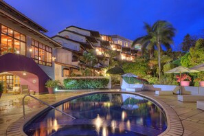A swimming pool with a clear view of the surrounding architecture, including a multi-story building with balconies and a landscaped garden with palm trees. - Alta Las Palomas Hotel  (Santa Ana)