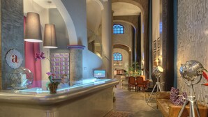 A reception area with a counter, a digital screen, and a seating area with a sofa and chairs. - Alta Las Palomas Hotel  (Santa Ana)