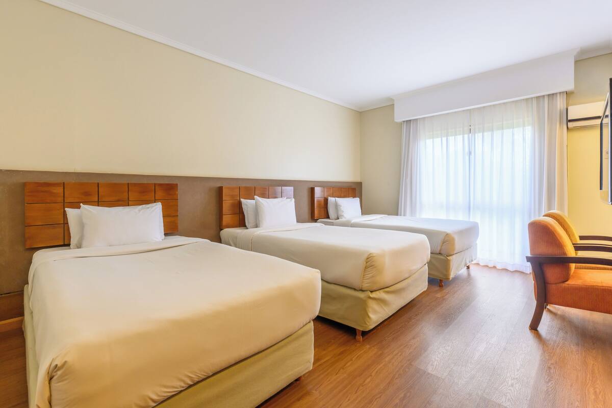 A hotel room with two beds, a wooden headboard, a chair, and a large window with curtains.