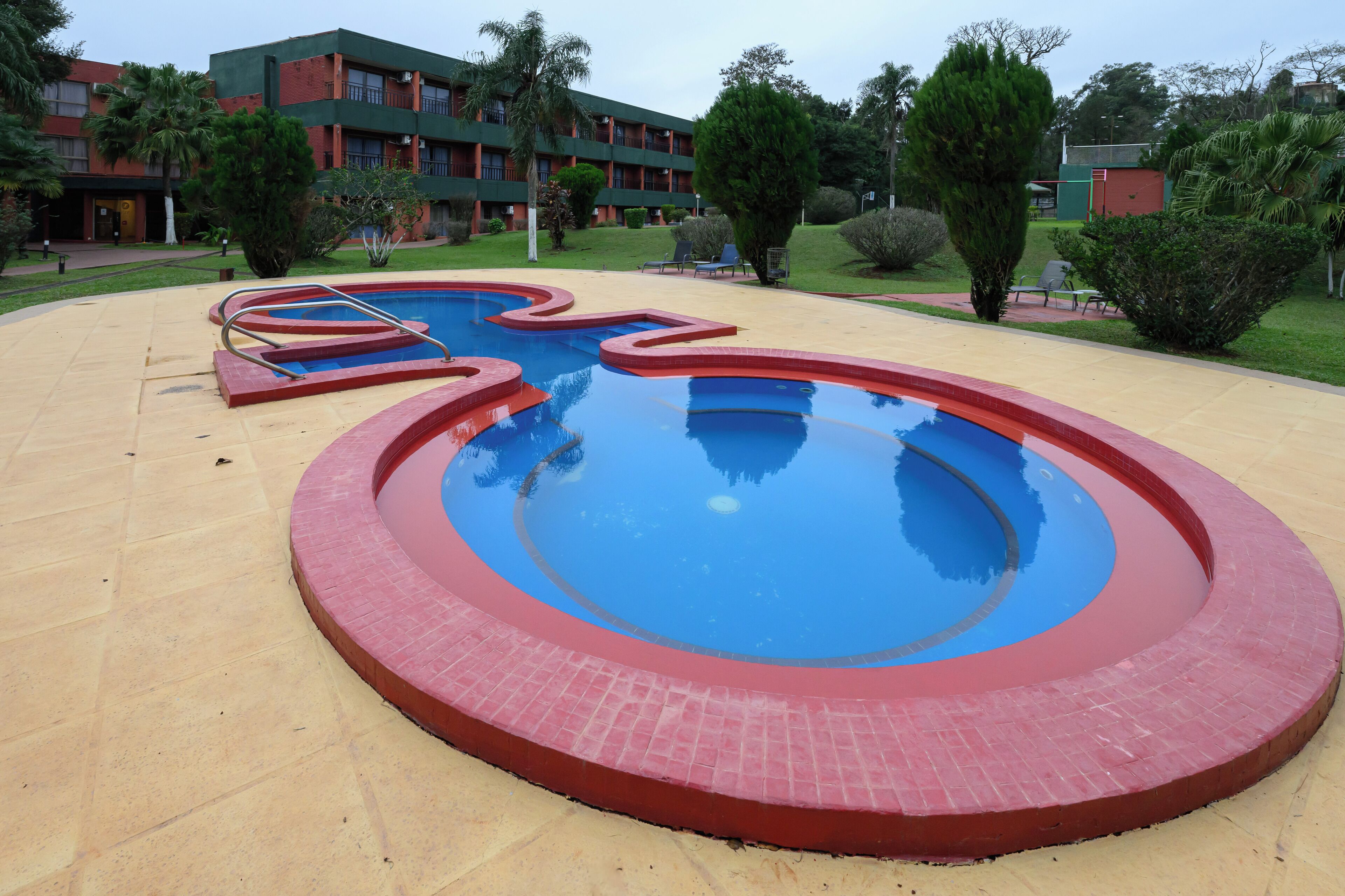 Une piscine aux motifs rouges et bleus, entourée d’une terrasse de couleur beige.