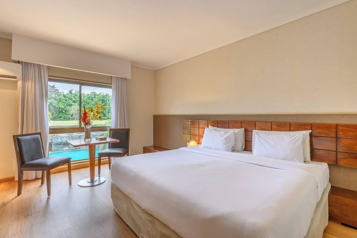 A hotel room with a large bed, a desk with a chair, and a view of a swimming pool.