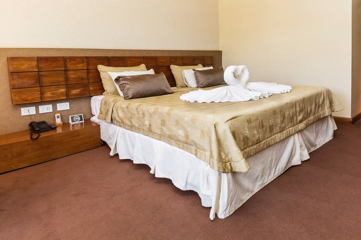 A neatly made bed with a headboard, a bedside table with a phone and a small item, and a wall socket.