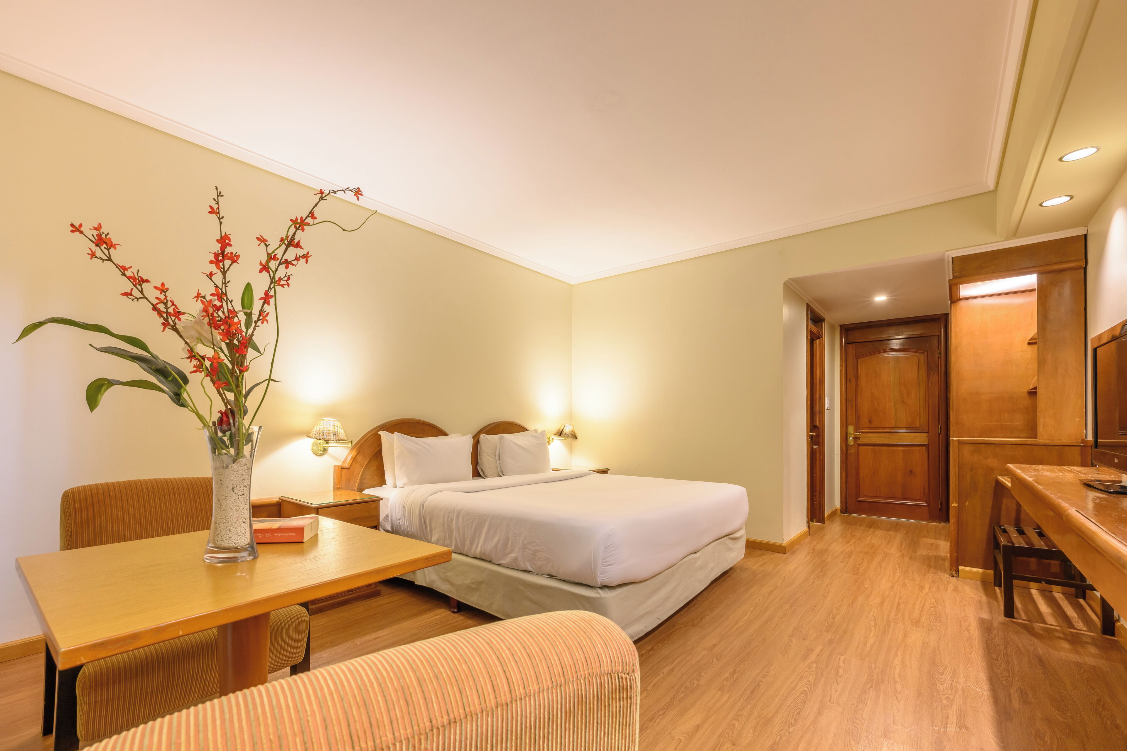 Een hotelkamer met een bed, nachtkastje, lamp en een tafeltje met een bloevas.