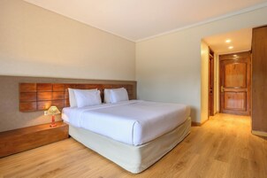 Un letto rifatto con cura in una camera d'albergo, con una testiera in legno, un comodino con una lampada e una porta in legno.