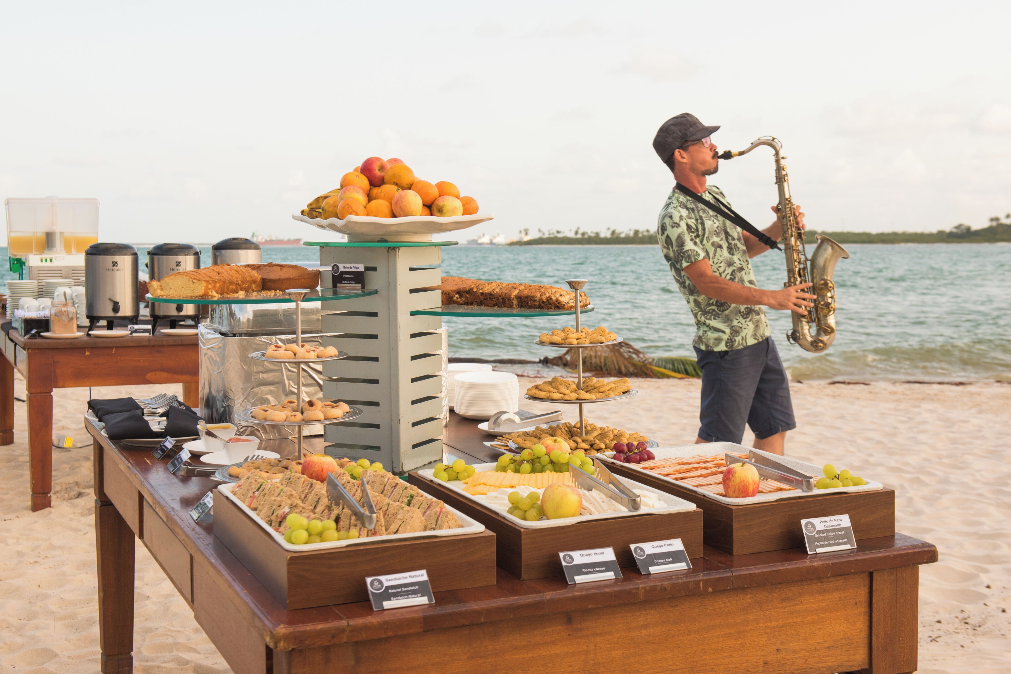 A buffet setup with various food items and a person playing a saxophone on a beach.