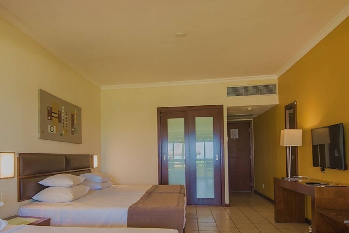 A hotel room with two beds, a desk, a TV, and a door leading to a balcony.