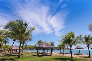 A beach with palm trees, thatched-roof structures, and a clear blue sky. - Vila Galé Cabo – All Inclusive (Cabo de Santo Agostinho)