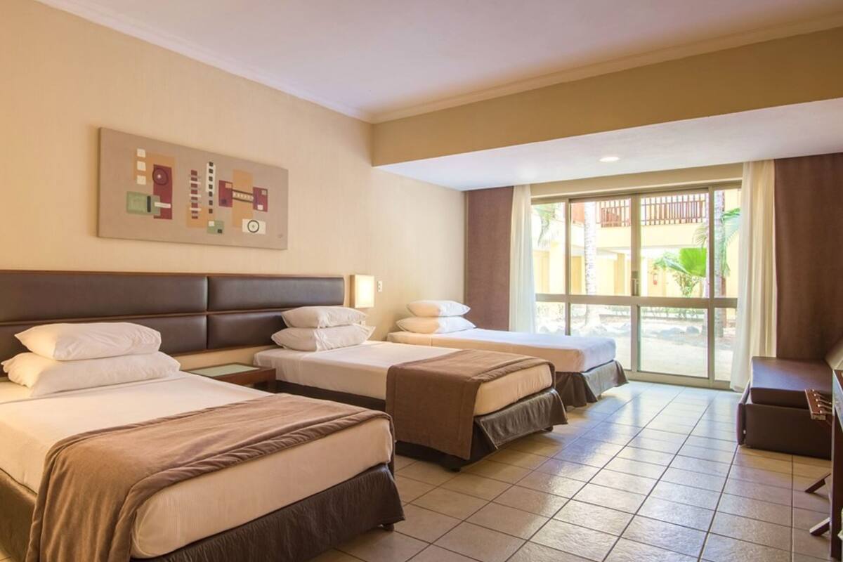 A hotel room with two beds, a desk, a chair, and a large window.
