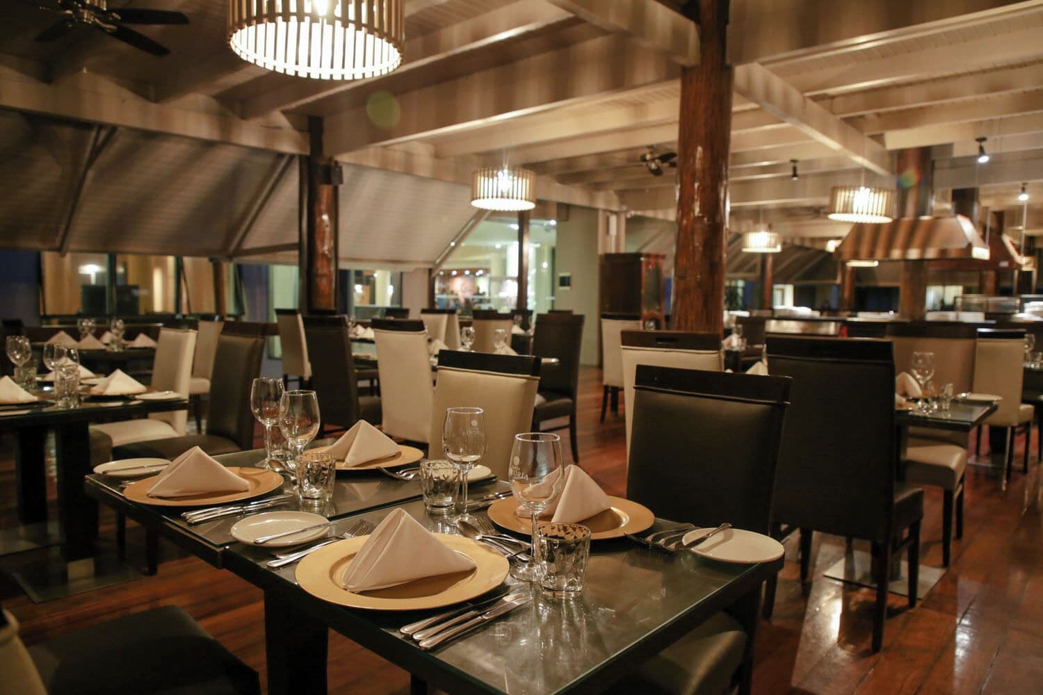Un restaurant avec des tables dressées pour le service, des chaises et des lampes suspendues.