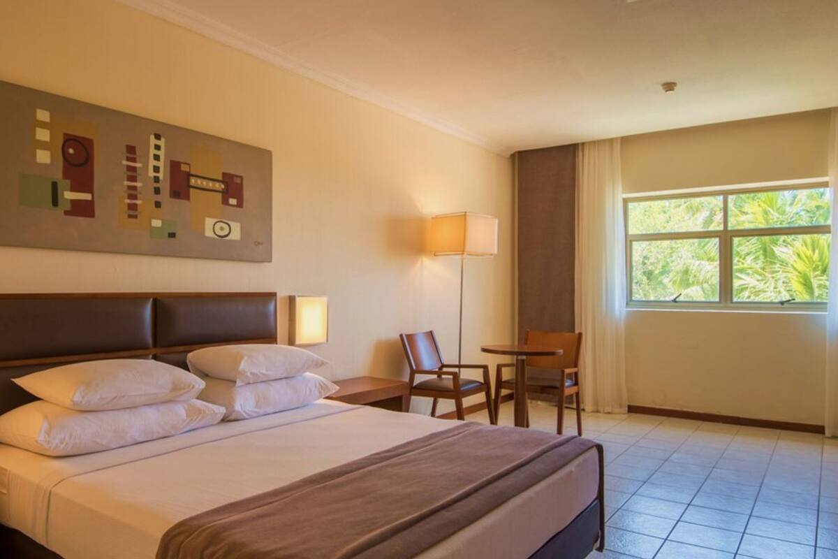 A hotel room with a large bed, a desk with a telephone, a chair, a table, and a window with curtains.
