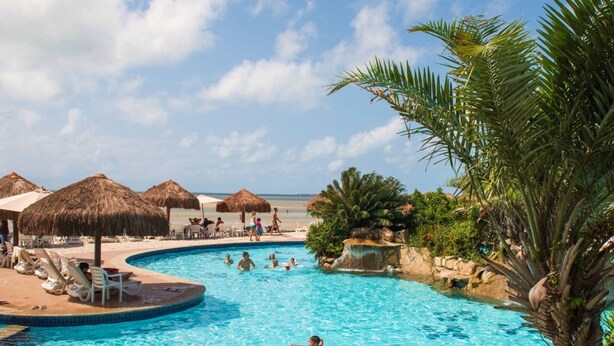 Un espace piscine avec des chaises longues et des parasols, une petite cascade et une vue sur la plage.